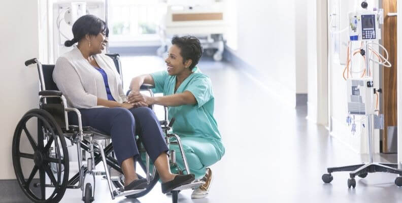 Nurse Kneeling Next to Patient in Wheelchair